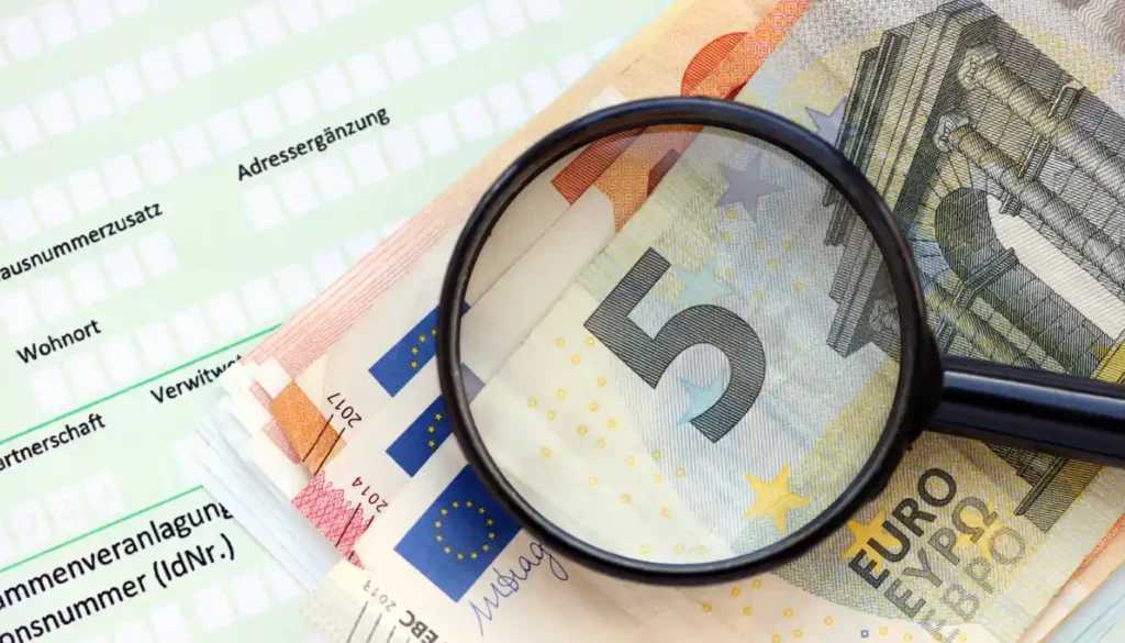 Geldscheine und eine Lupe auf einer Steuererklärung – symbolisiert den Einfluss der Grundsteuer auf die Bewertung von Immobilien